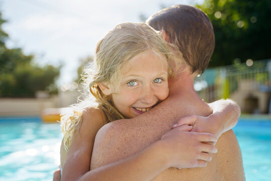 Smiling blond girl embracing father in swimming pool