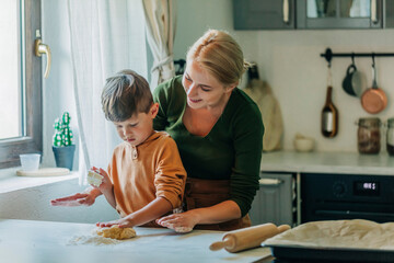 Mother and son kneading dough in kitchen at home