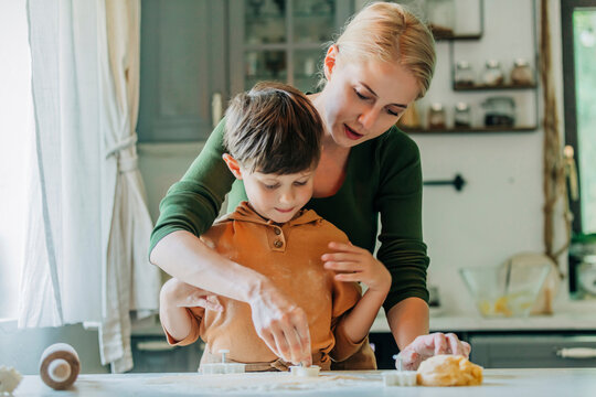 Mother and son cutting dough with cookie cutter in kitchen