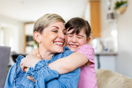 Smiling mother and daughter with eyes closed embracing at home