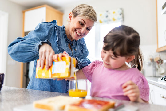 Happy mother helping daughter to pour juice in glass at home