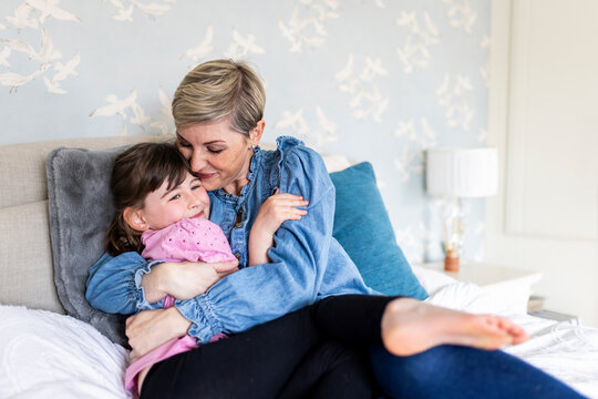 Mother hugging daughter lying on bed at home