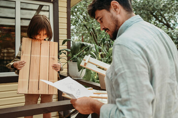 Father reading instruction manual and son holding wooden plank in back yard