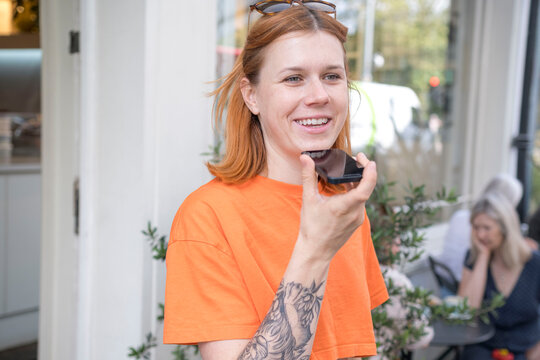Smiling woman sending voicemail through mobile phone at sidewalk cafe