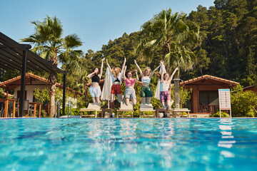 Cheerful friends jumping near swimming pool