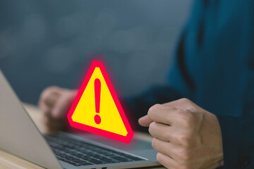 Businessman using laptop showing warning triangle and exclamation sign icon Warning of dangerous...
