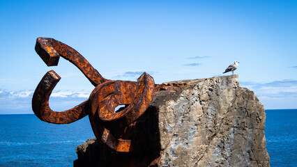 Fototapeta premium A seagul standing on a rock looking at the sea with some old pieces of metal