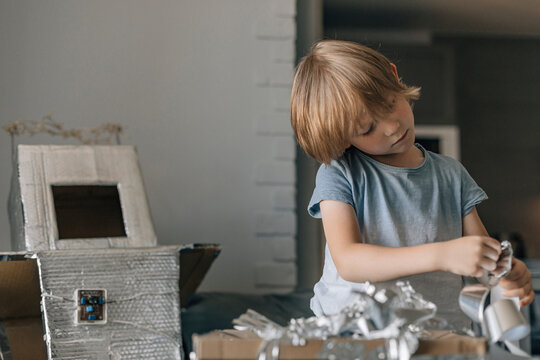 Focused boy with silver foil paper making astronaut costume