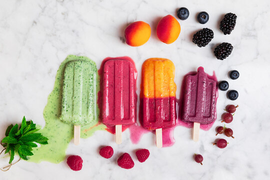 Berry fruits and melting popsicles on marble surface