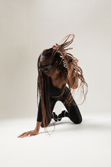 Young African American woman with long braids posing on white wall. Vertical.