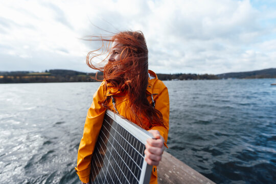 Redhead woman holding solar panel at lake