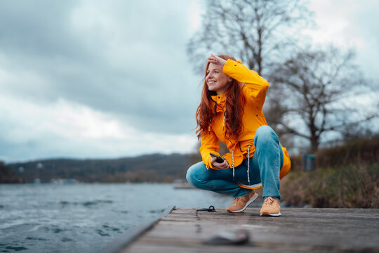 Smiling woman squatting on pier by lake