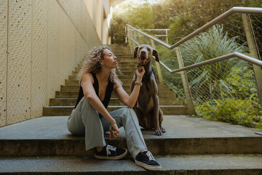 Young Woman Stroking Dog Sitting On Steps