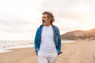 Senior man with hands in pockets walking at beach
