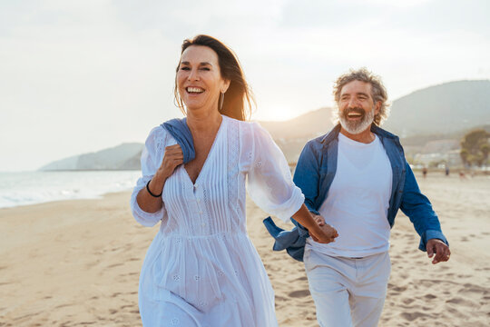Happy woman holding hands with man walking at beach