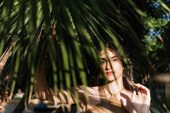 Young woman between palm leaves on sunny day