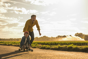 Happy boy enjoying skateboarding by grandfather on sunny day
