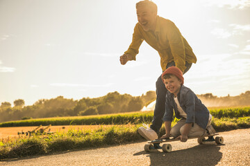 Cheerful grandson having fun and skateboarding by grandfather