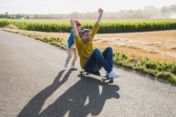 Happy boy pushing grandfather on skateboard on road