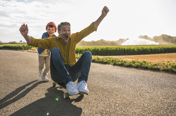 Cheerful man getting pushed by grandson on skateboard