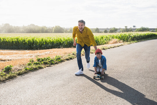 Happy grandfather pushing grandson on skateboard on road