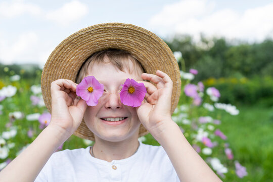 Happy boy holding pink flowers over eyes in garden - Powered by Adobe