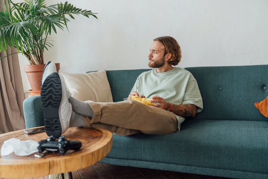 Thoughtful young man with snacks sitting at home