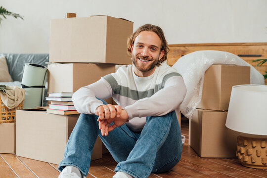 Happy young man sitting with hands clasped by cardboard boxes