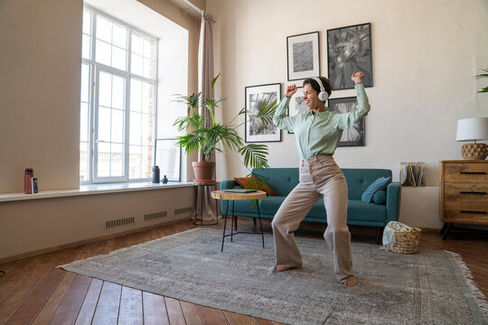 Cheerful woman wearing wireless headphones dancing at home