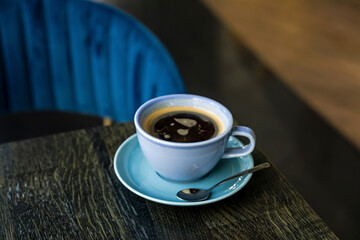 A blue ceramic cup of hot black coffee close-up on a wooden table, atmosphere of a cafe, copy space - 644374144