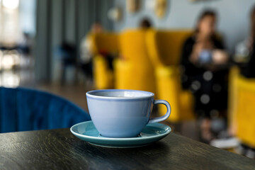 Blue ceramic cup of hot black coffee on wooden table, cafe atmosphere, people in bokeh, copy space