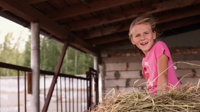 Cute little girl in pink t shirt sitting outdoors in strong wind smiling, little girl sit on a stock of hay and enjoying wind in her hair