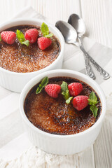 Chocolate creme brulee with caramel crust garnished with mint and raspberries close-up in ramekin on the table. Vertical
