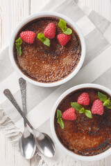 Chocolate creme brulee with caramel crust garnished with mint and raspberries close-up in ramekin on the table. Vertical top view from above