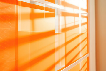 A vibrant orange background with a bold geometric pattern in contrasting shades. The sunlight peeks through a window covered with translucent blinds, creating playful shadows that mimic