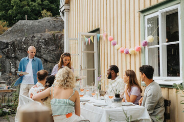 Smiling woman serving food to male and female friends during dinner party at cafe