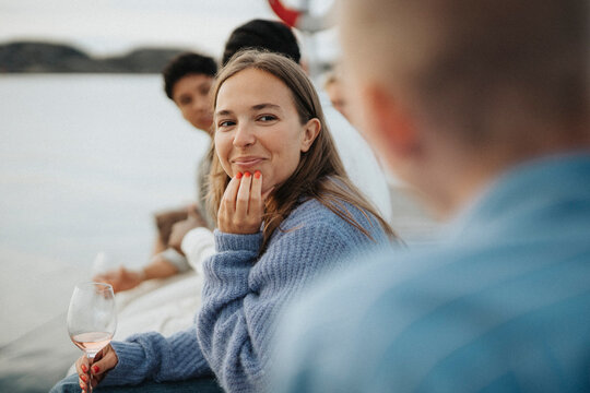 Smiling young woman with hand on chin sitting with friends on pier near lake