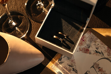 The wedding rings of the bride and groom made of white gold are in a velvet box. Wedding. The engagement. The bride's shoes. Champagne glasses on a dark background.
