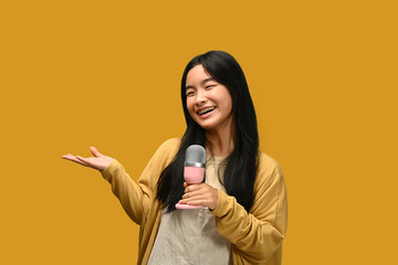 Happy teenage girl singing songs with microphone, posing isolated on yellow background