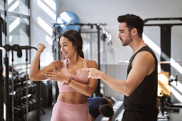 Fototapeta na wymiar Fitness woman showing her muscle to her personal trainer after working out in the gym. Sports concept.