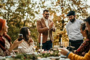 The joyous ambiance of a garden party, with a diverse group of people relishing a shared meal amidst nature's beauty.