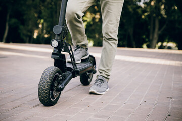 A man's foot stands on the platform of a scooter. Close-up of a man riding a black electric scooter. Walking and outdoor sports. Economical and environmentally friendly appliances for transportation.