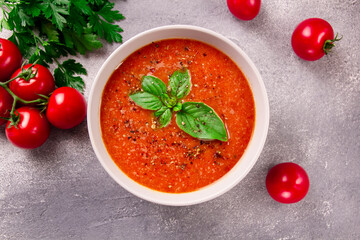 Tomato cream soup with basil and spices on gray background