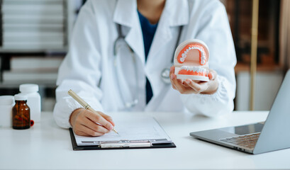 Concentrated dentist sitting at table with jaw samples tooth model and working with tablet and...
