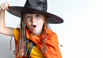 happy little girl with pigtails dreadlocks with pumpkin in witch costume, black hat laughs,...