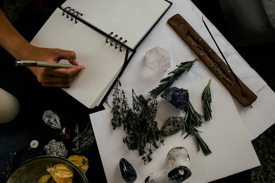 Cropped image of woman writing in book by herbs and crystals on table