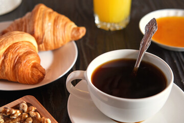 Coffee cup with croissant on a rustic dark wooden table. Food series. Two tasty fresh croissants, jam, orange juice. Continental breakfast served with freshly baked pastry. Close up view, Good morning