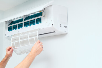 Air conditioner service indoors. Male Technician removing air filter of the air conditioner for cleaning.