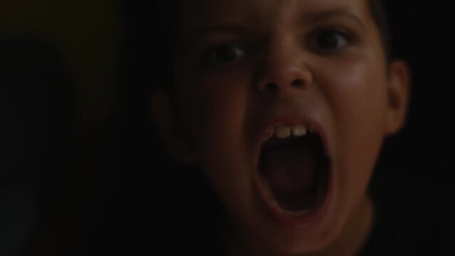 Child's face and hands frightening and screaming in the dark