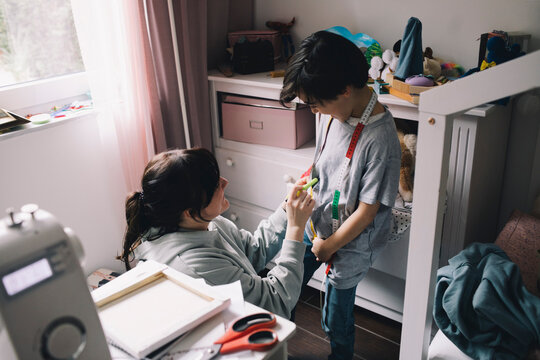 Mother using tape measure while sewing clothes for son at home